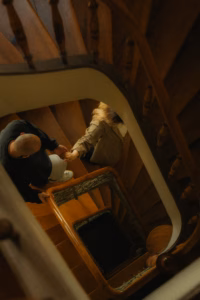 Couple walking down a wooden spiral staircase, viewed from above, warm lamplight