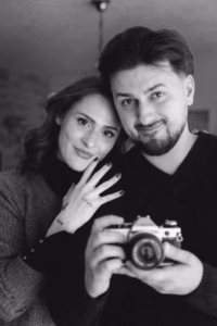 Close-up black-and-white portrait of a couple, cheek to cheek, with him holding a vintage camera.