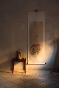 Hanging scroll painting of flowers lit by a shaft of light, with a small wooden side table beneath it
