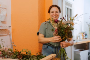 Smiling woman holding a finished bouquet in a flower shop with an orange wall