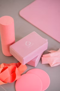 Flat lay of pink Pilates equipment: foam roller, yoga block, resistance bands, and small balls