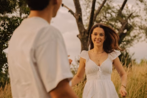 Woman in a white dress smiling and walking toward her partner in a golden field