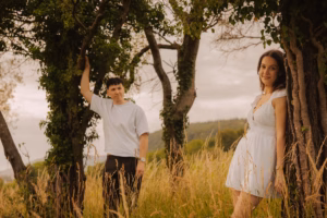 Couple standing among trees in a golden grass field, hills in the background