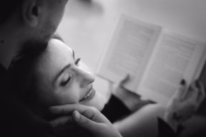 Black-and-white portrait of a woman leaning back against her partner while reading a book