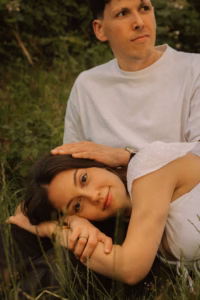 Woman lying in grass with her head resting near her partner's hand, who sits behind her