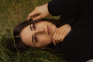 Woman with dark hair lying in grass, one hand resting near her face