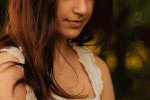 Close-up of a woman with long brown hair in a white top, smiling softly in golden evening light