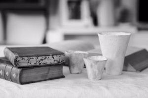 Black-and-white still life of ceramic cups beside a stack of old books