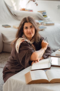 Woman sitting at a table surrounded by open books, looking at the camera